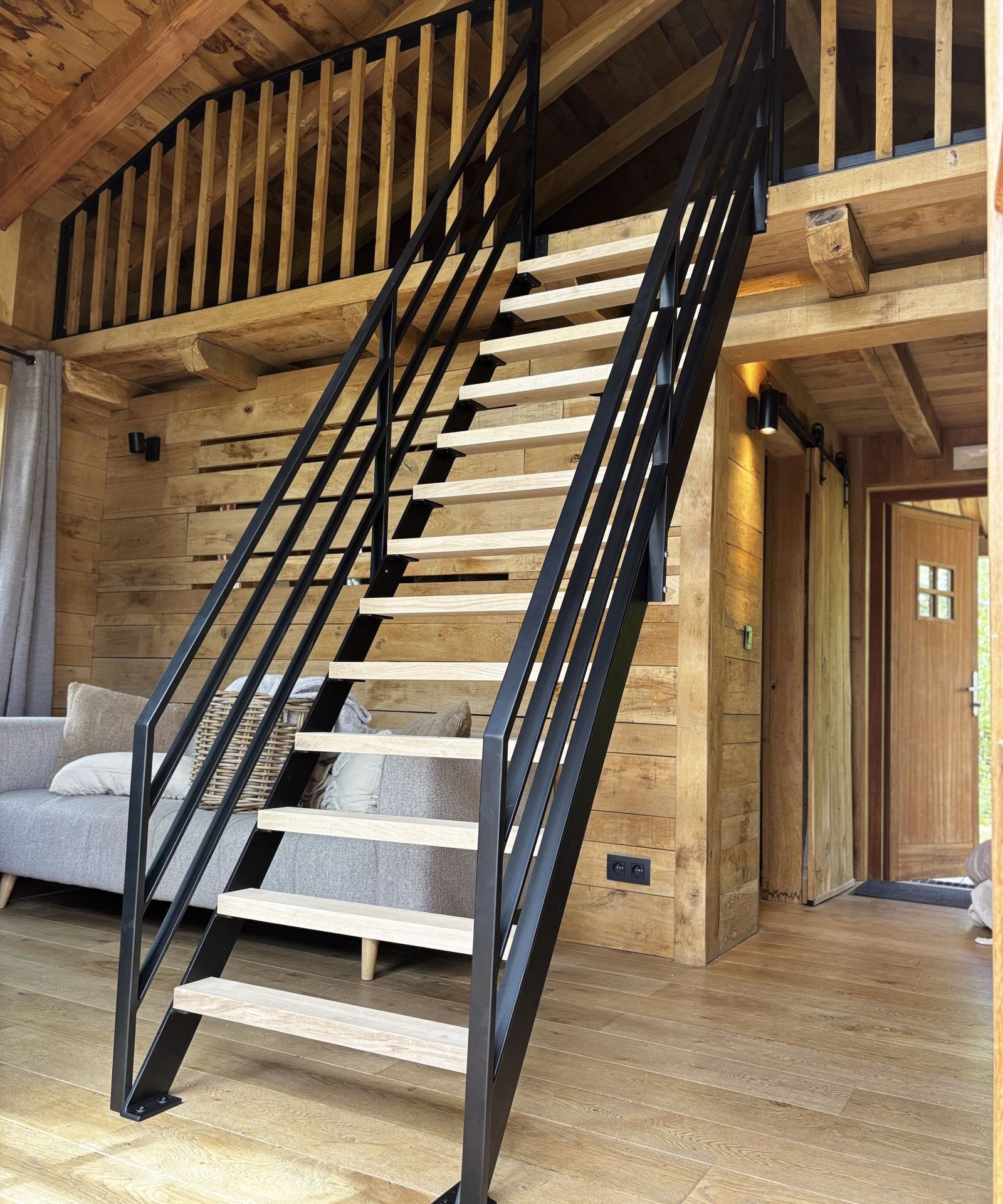 Escalier en acier noir à marches claires et garde-corps à barres, dans un chalet en bois