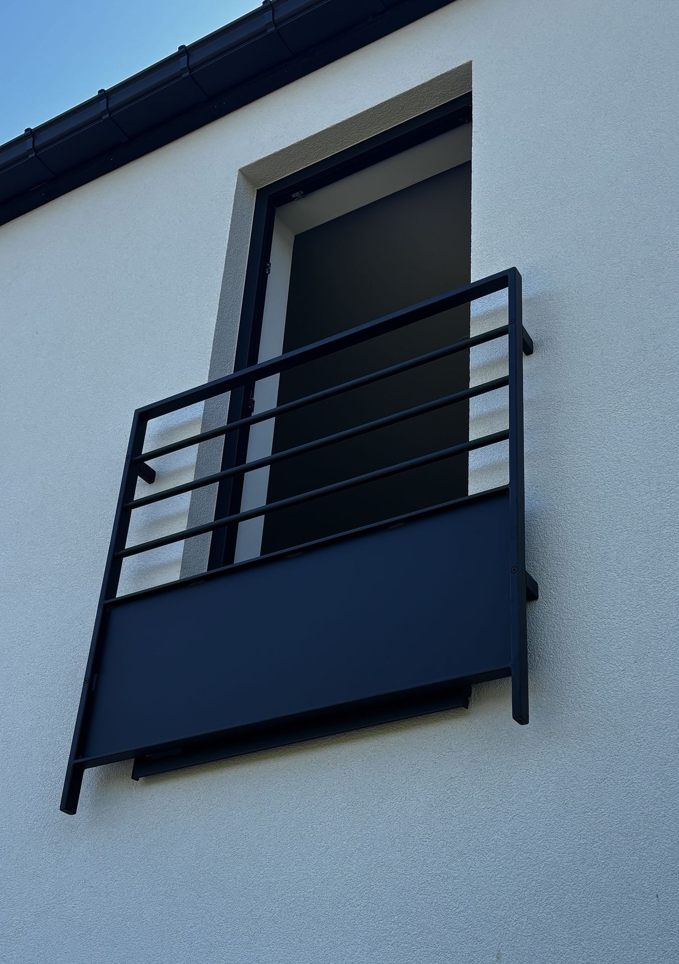 Garde-corps de fenêtre en acier thermolaqué noir, barres horizontales et panneau plein, façade enduite blanche