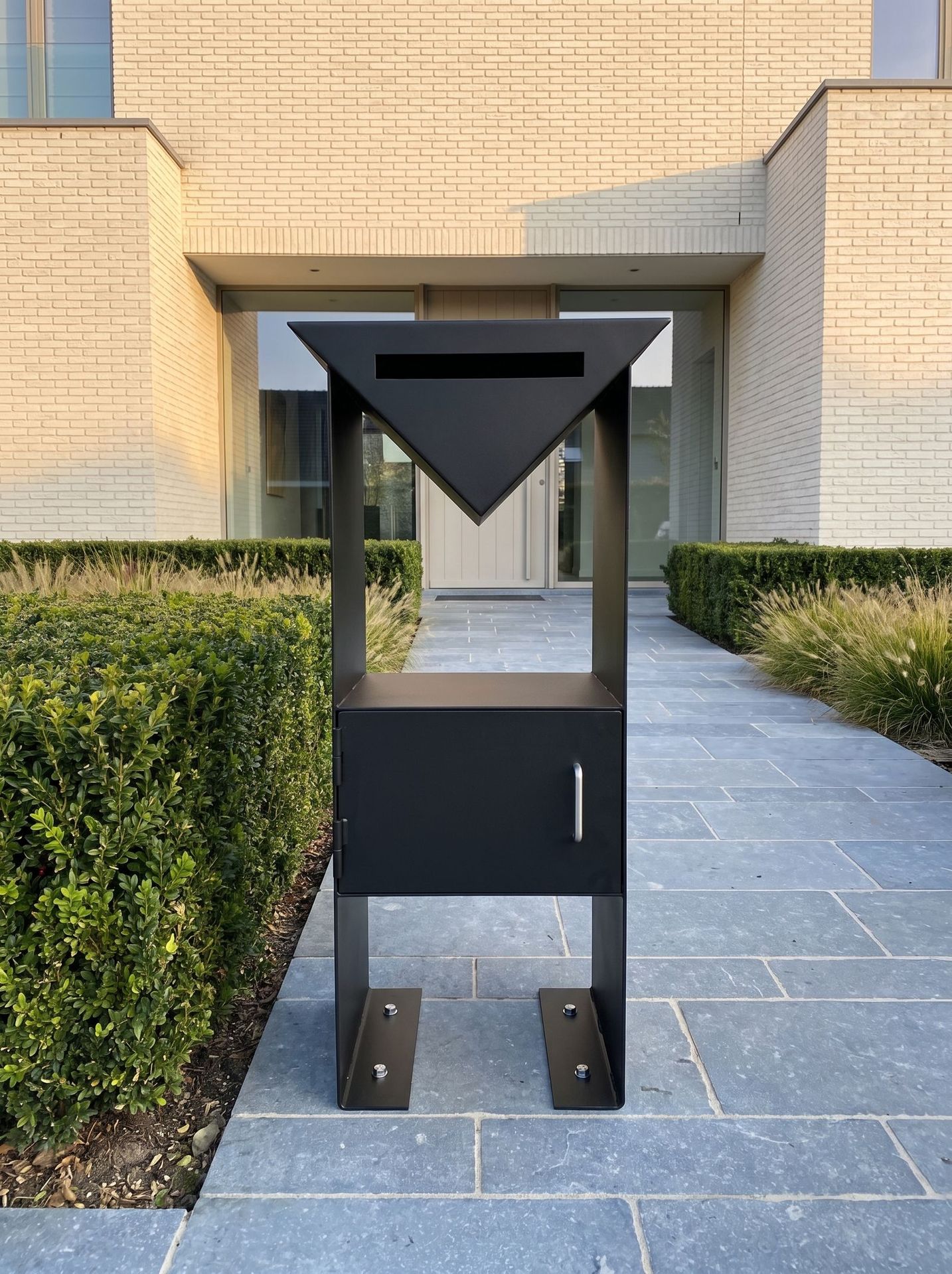 Mise en situation (décor créé par IA) : boîte aux lettres sur mesure en acier noir sur colonne, devant une maison contemporaine