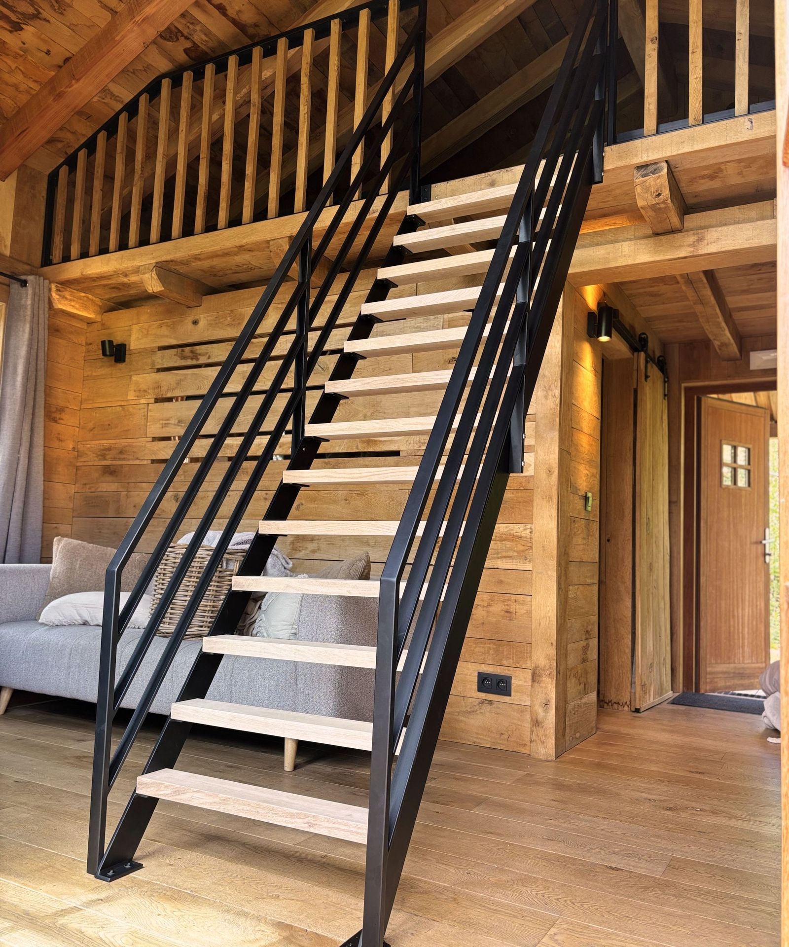 Escalier en acier noir à marches claires et garde-corps à barres, dans un chalet en bois